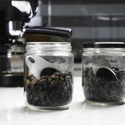 Jar of dark coffee beans with stainless-steel scoop-shaped insert