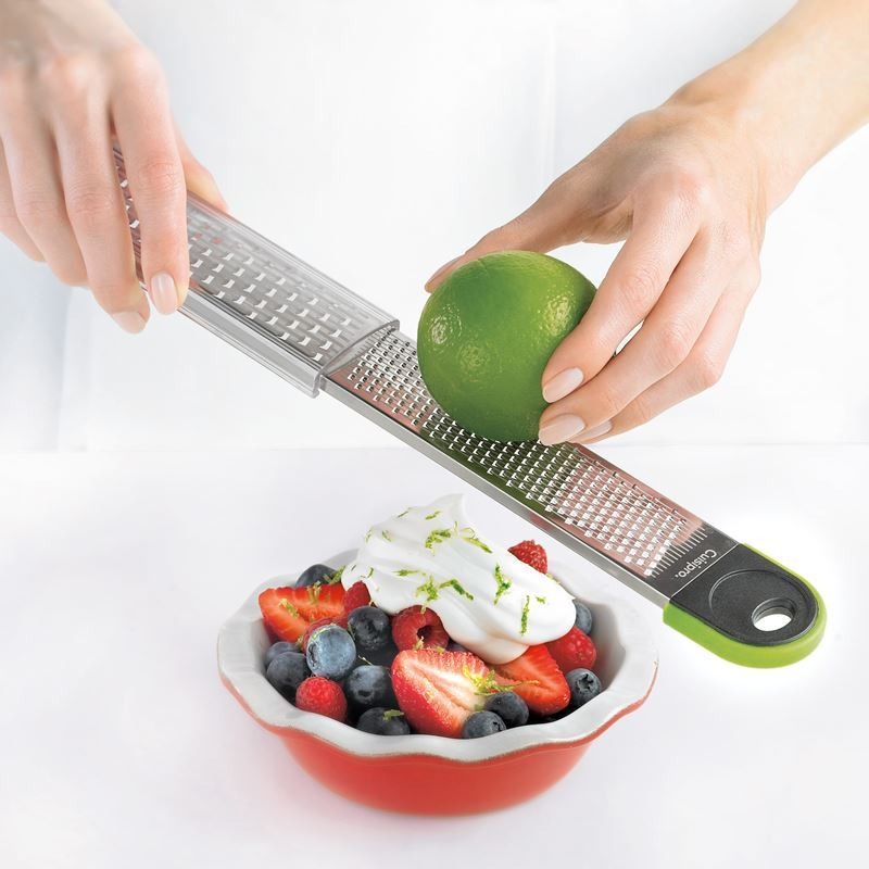 Dual grater held above fruit and berries, showing stainless grating surface