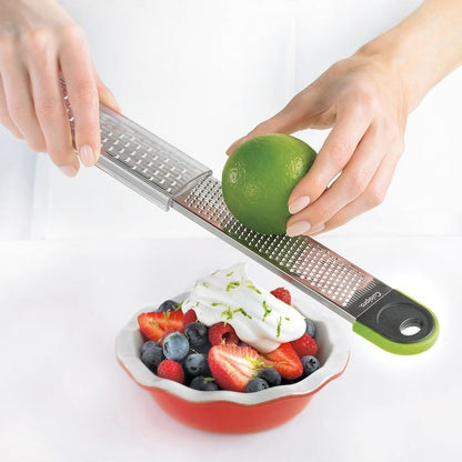 Dual grater held above fruit and berries, showing stainless grating surface