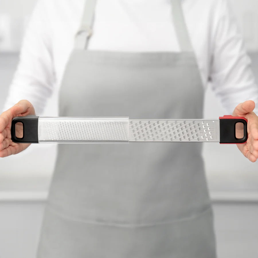 Grater held horizontally by hands over a white apron