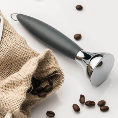 Coffee tamper with dark handle and chrome head beside coffee beans