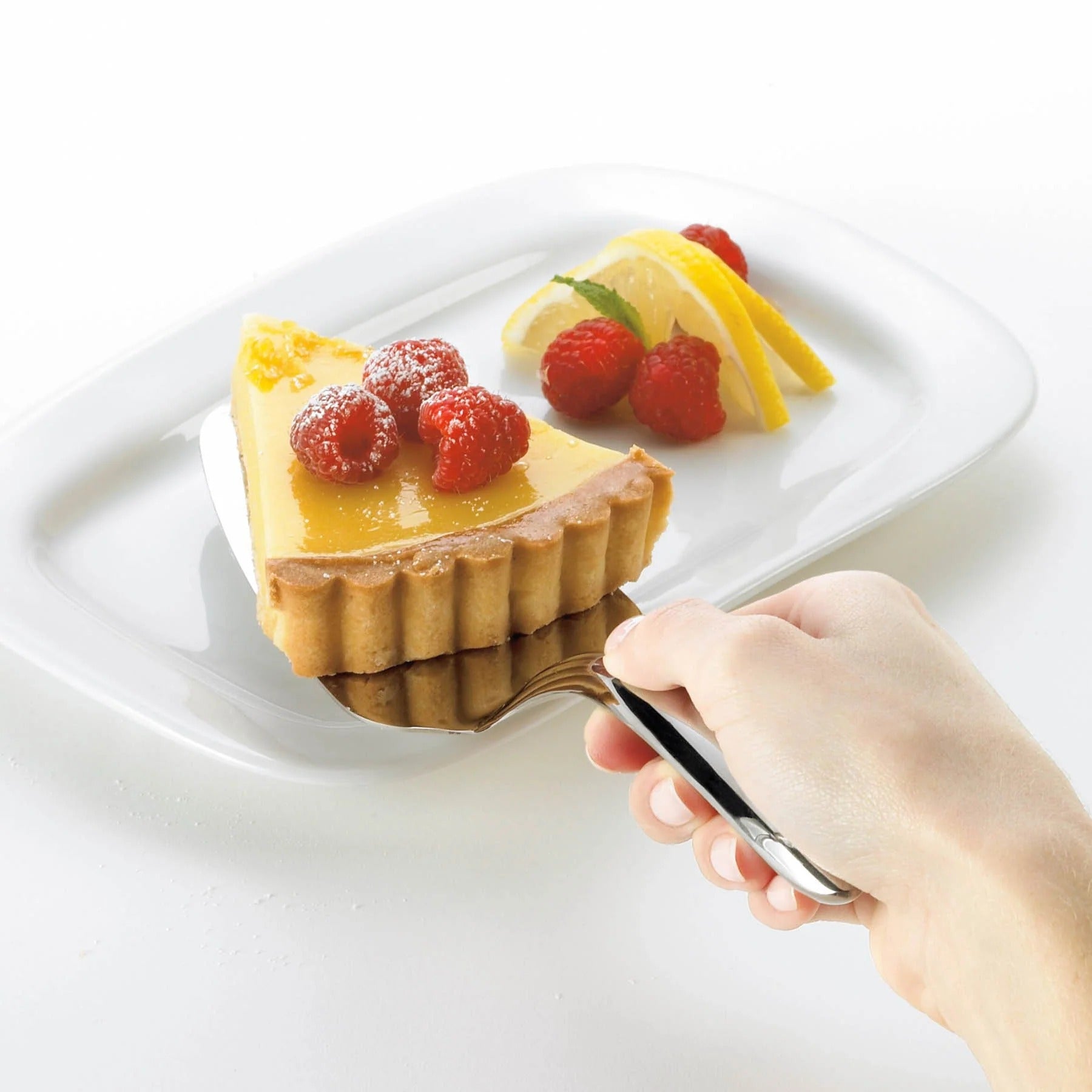 Mini cake/pie server lifting a small tart with berries and lemon garnish