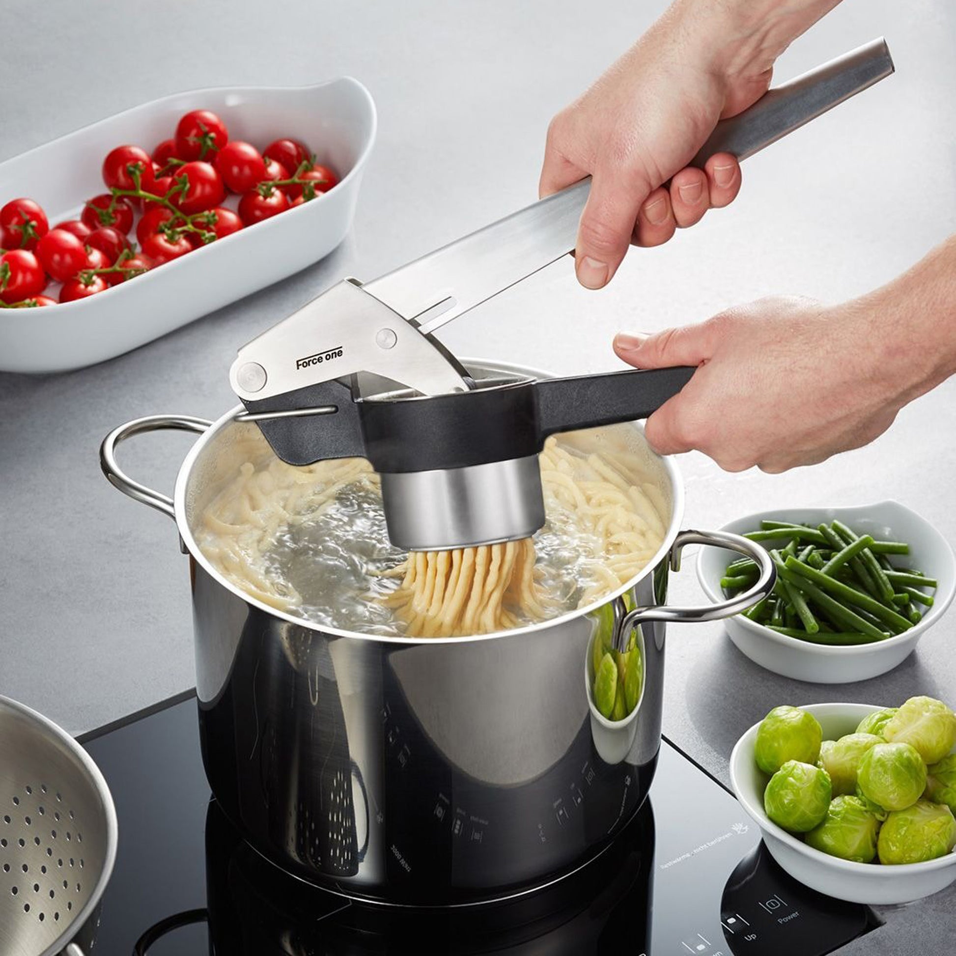 Potato, juice & spaetzle press extruding pasta dough into a pot, with hands