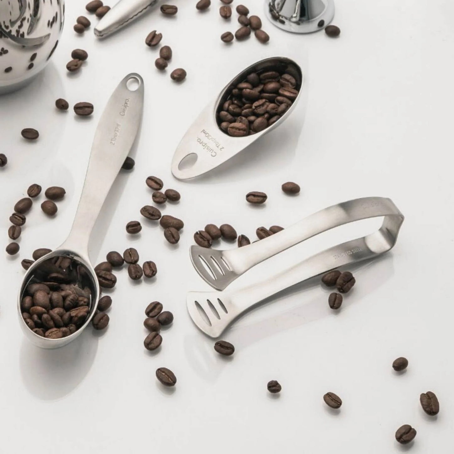 Pair of stainless steel tea bag tongs lying on a countertop with coffee beans